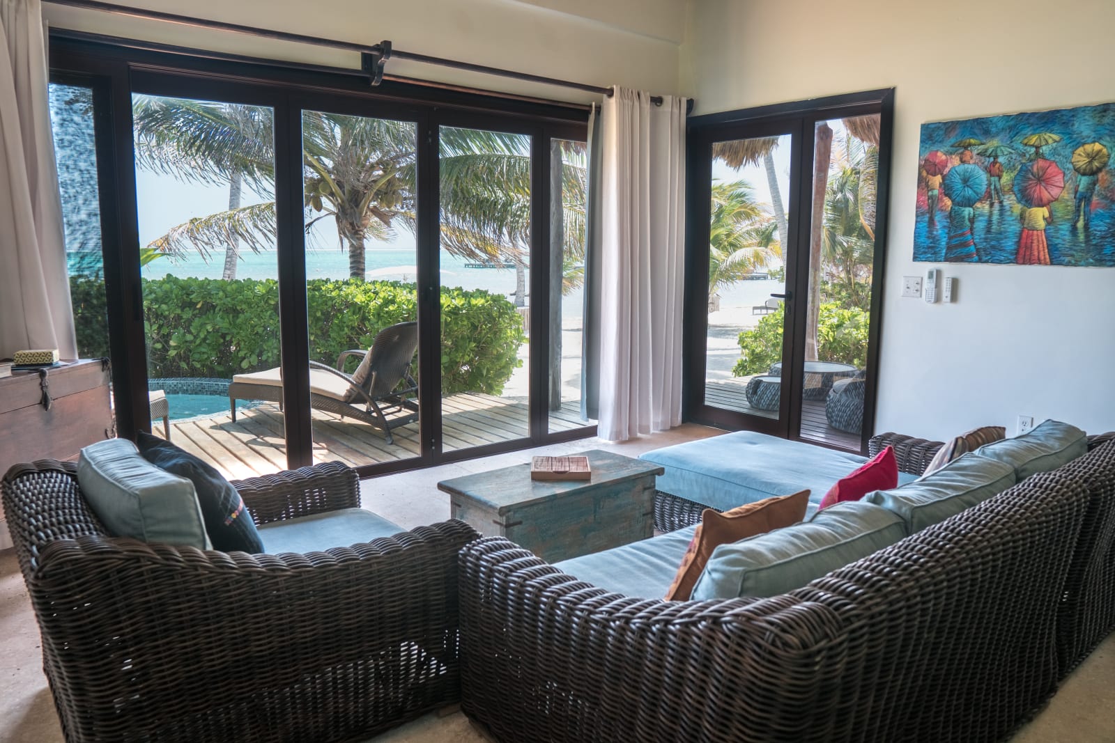 Interior of a Matachica suite with wicker seating opening through folding glass doors onto a private terrace, plunge pool, and Caribbean view, Ambergris Caye, Belize