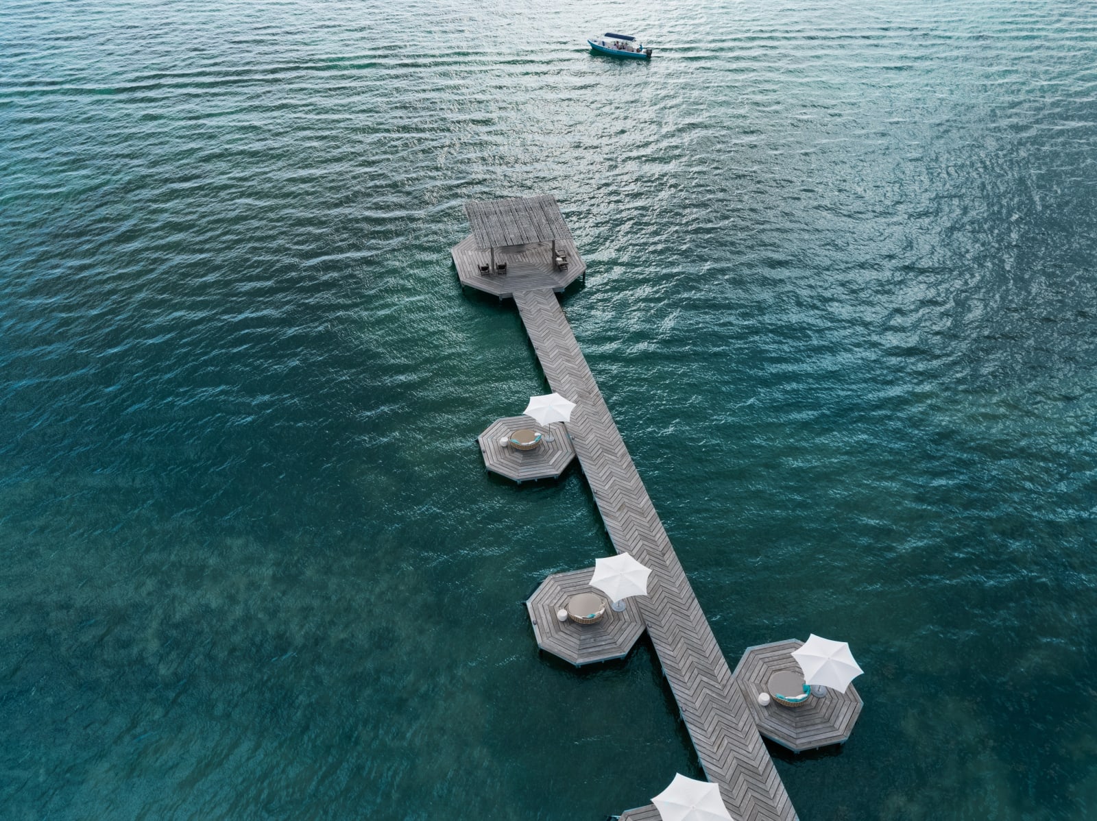 Overhead view of Matachica's herringbone-planked pier with octagonal lounge platforms and white umbrellas over the deep blue Caribbean, Ambergris Caye, Belize