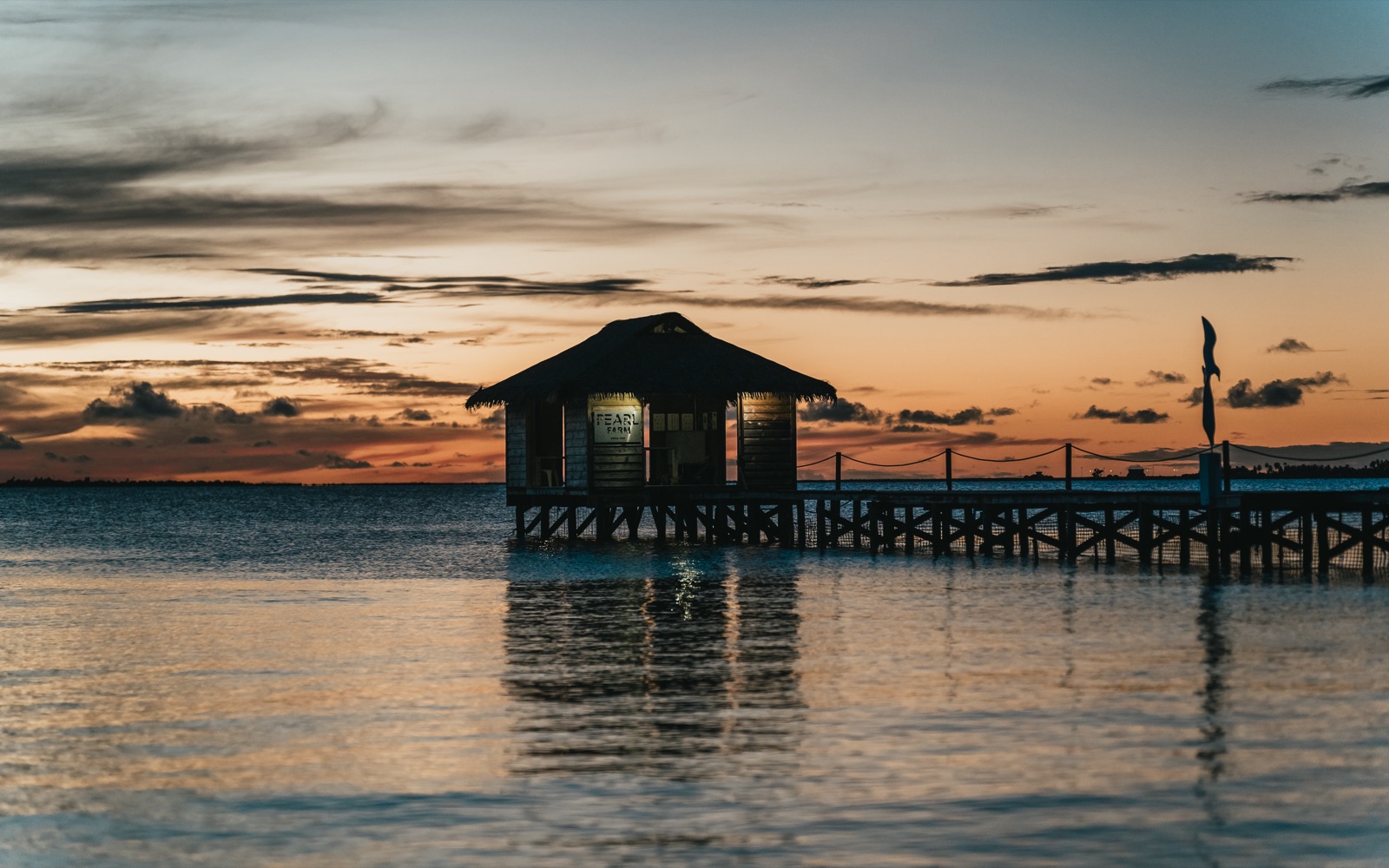 Havaiki Lodge's over-water Pearl Farm hut glowing at dusk at the end of its wooden jetty over the Fakarava lagoon